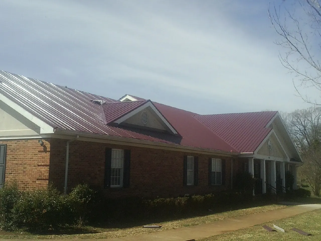 Red metal roof with gabled entries on a long brick building, from a Hail Damage Roof Repair job in Algodones
