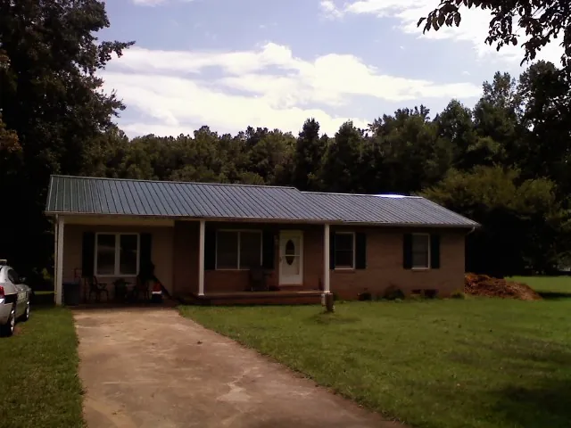 Dark green metal roof on a brick ranch with a covered porch in Algodones