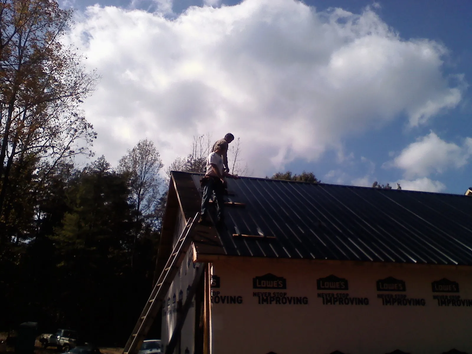 Roofer fastening dark metal panels high against a cloudy sky, from a Roof Inspection job in Algodones